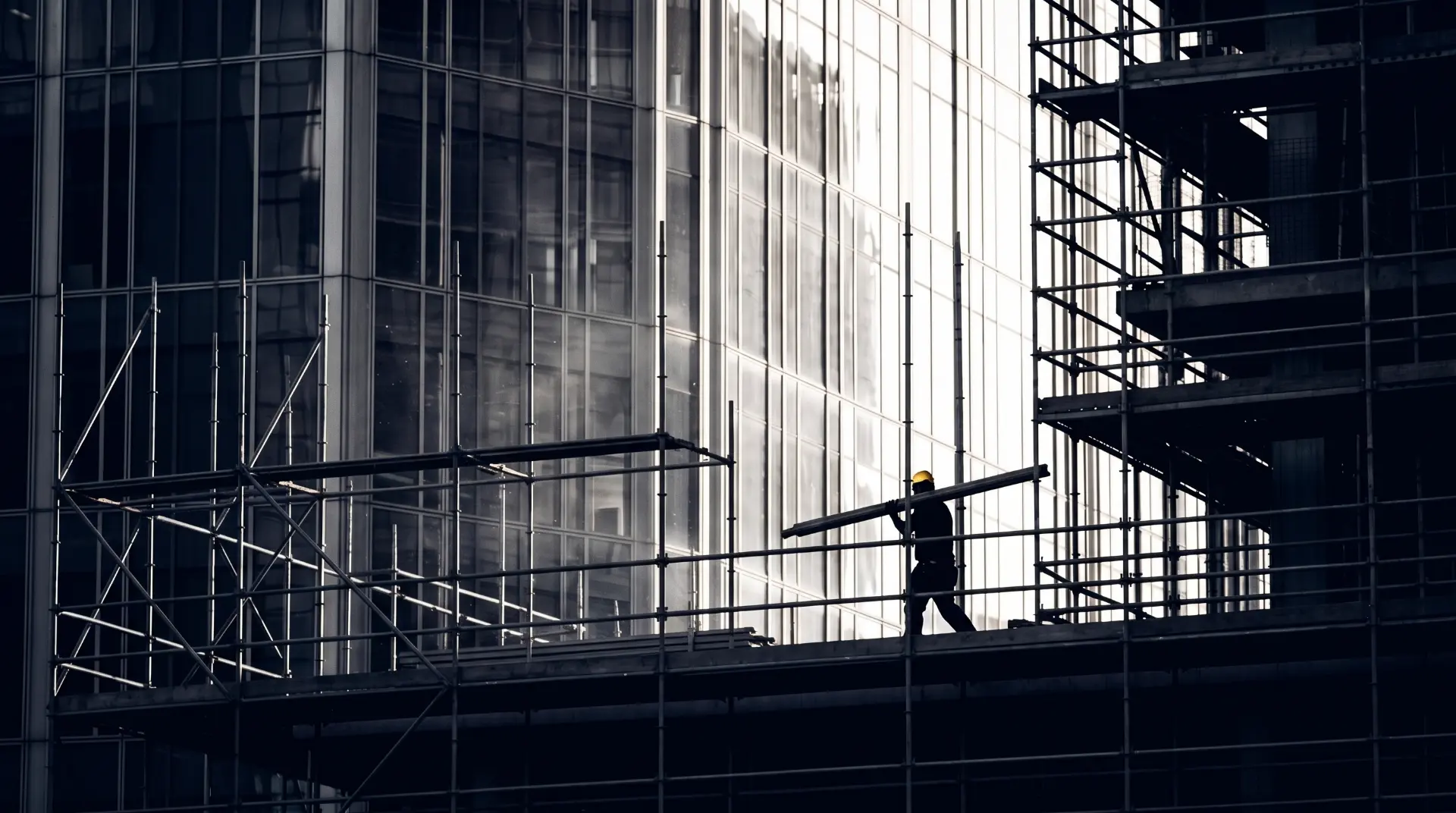 Worker carrying a beam across scaffolding on a glass building